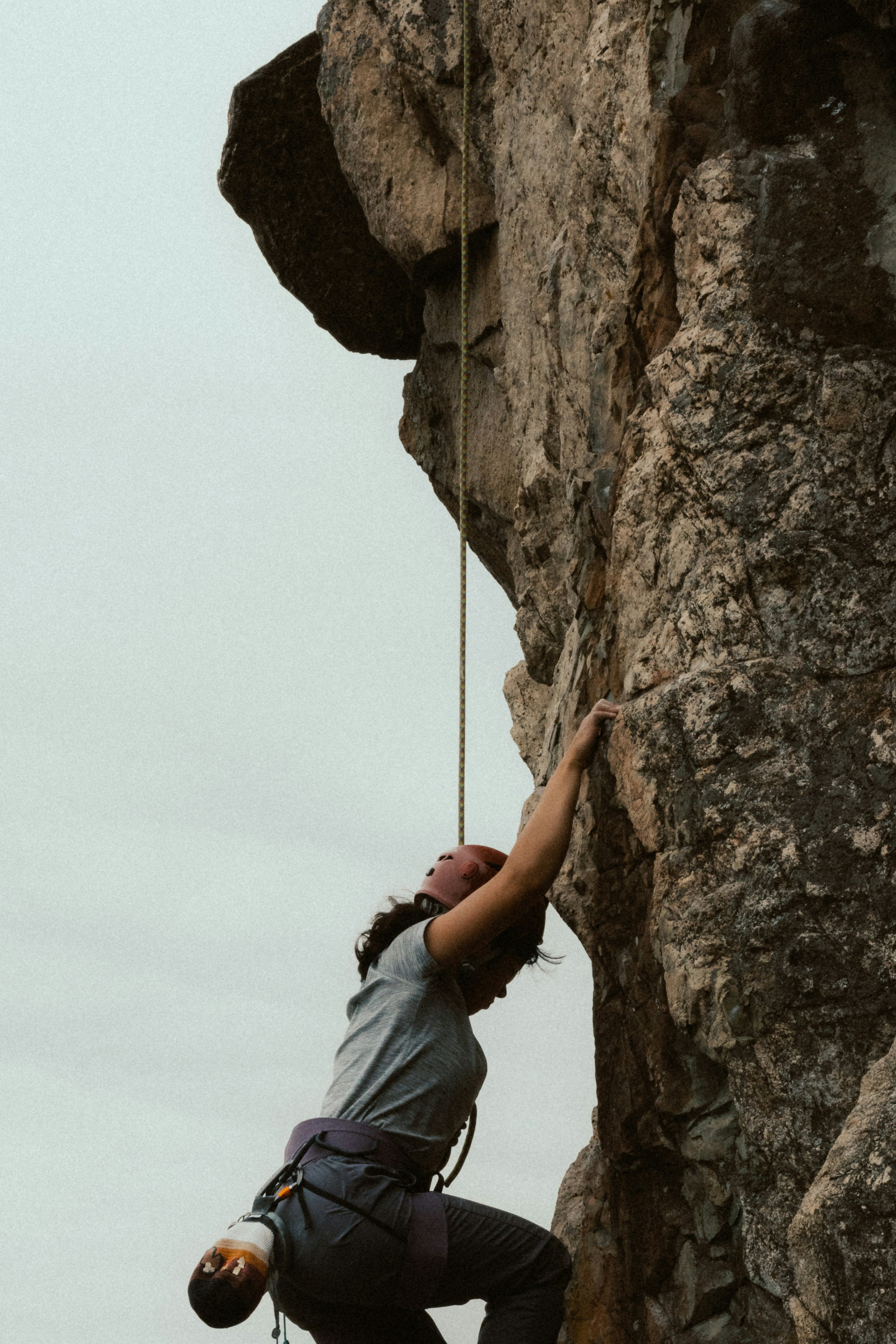 Person climbing a rocky cliff face with a rope.